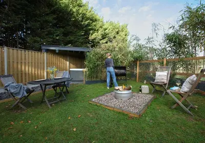 a man standing in a backyard with a table and chairs at Sycamore Lodge with Hot Tub- Quirky & Romantic in Halstead