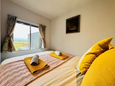 a bedroom with a bed with yellow pillows and a window at Unique Suffolk Cabin with Countryside Views in Burgh