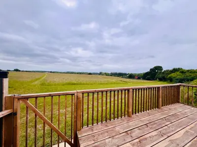 a wooden deck with a view of a field at Unique Suffolk Cabin with Countryside Views in Burgh