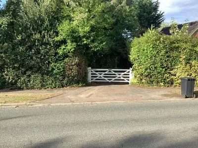 a driveway with a white gate and some bushes at The Eclectic Coach House in Roydon