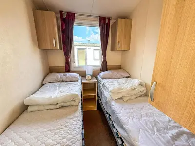two beds in a small room with a window at Cosy Caravan With Decking At Oaklands Holiday Park In Essex Ref 39042Cf in Clacton-on-Sea