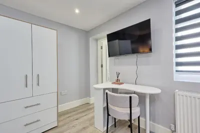 a white room with a table and a tv on the wall at Studio By Homestyles Hosts Short Lets & Serviced Accommodation Widford - Free WiFi in Writtle
