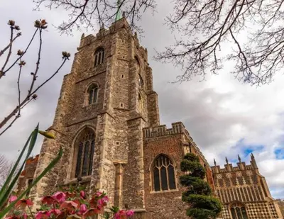 an old stone church with a tower with pink flowers at Studio By Homestyles Hosts Short Lets & Serviced Accommodation Widford - Free WiFi in Writtle