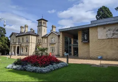 a large brick building with a clock tower and flowers at Studio By Homestyles Hosts Short Lets & Serviced Accommodation Widford - Free WiFi in Writtle