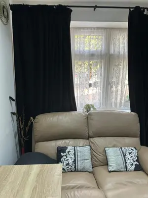 a leather couch with pillows in front of a window at A Comfortable and Cosy Self Contained Room in Navestock