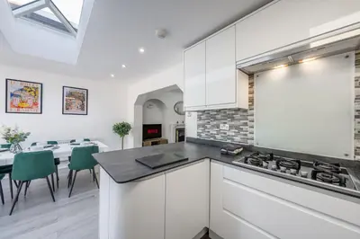 a kitchen with white cabinets and a table with green chairs at Free parking - 6 Bedroom Home in Colchester
