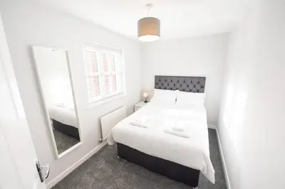 a small white bedroom with a bed and a mirror at Two Double Bed Coach House with Parking Fast WiFi in Colchester