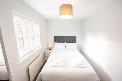 a white bedroom with a bed and a window at Two Double Bed Coach House with Parking Fast WiFi in Colchester