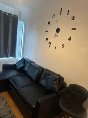 a black leather couch in a living room with a clock on the wall at The Retreat On Retreat Road in Southend-on-Sea