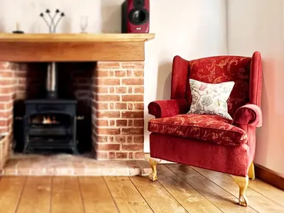 a red chair with a pillow in front of a fireplace at Brick Kiln Holdings by The Suffolk Cottage Collection in Badingham