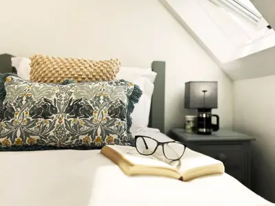 a book and glasses on a bed with a pillow at Blackberry Barn by The Suffolk Cottage Collection in Long Melford