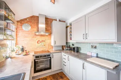 a kitchen with white cabinets and a brick wall at Market View, Framlingham in Framlingham