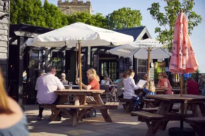 a group of people sitting at tables with umbrellas at The White Hart Inn in West Mersea