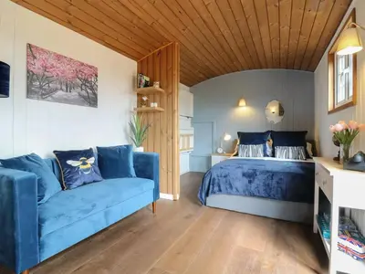 a bedroom with a blue bed and a blue couch at Luxury Shepherd Hut with Private Hot Tub in Swaffham Bulbeck
