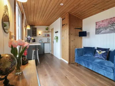 a living room with a blue couch and a kitchen at Luxury Shepherd Hut with Private Hot Tub in Swaffham Bulbeck
