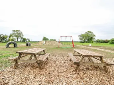 two picnic tables and a playground in a field at Luxury Shepherd Hut with Private Hot Tub in Swaffham Bulbeck