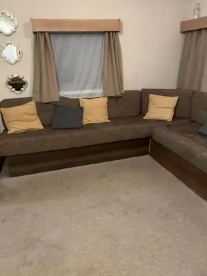 a couch with pillows and a window in a living room at 2 bed caravan seawick hoilday Park in Clacton-on-Sea