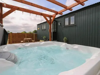 a hot tub in a backyard with a green building at Luxury Shepherd Hut with Private Hot Tub in Swaffham Bulbeck