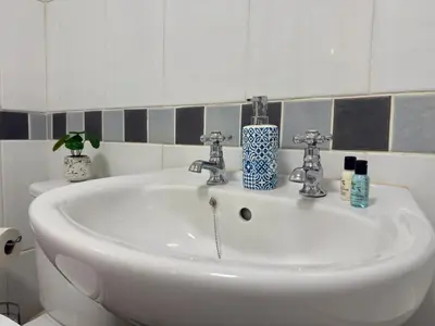 a bathroom sink with two faucets and bottles on it at 2 bed Elegant Flat in Stansted with parking in Stansted Mountfitchet