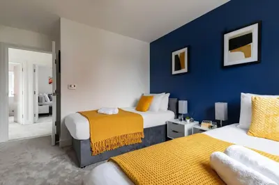 a bedroom with two beds and a blue wall at Beaulieu Rest 3 Bed House Chelmsford in Broomfield