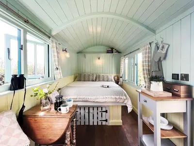 a bedroom with a bed and a desk and windows at The Hollies Shepherds Hut by The Suffolk Cottage Collection in Sutton