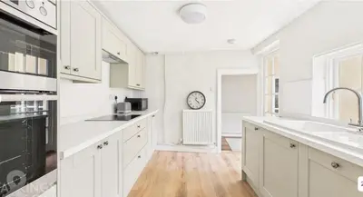 a kitchen with white cabinets and a clock on the wall at Courtyards, 9 Mount street,Diss in Diss