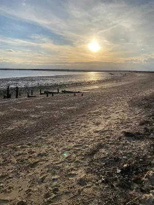 a beach with the sun setting on the water at Oyster Lodge in West Mersea