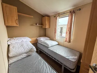 a small room with two beds and a window at Great 8 Berth Caravan With Unlimited Wi-Fi At Seawick Holiday Park, Ref 27213Sw in Clacton-on-Sea