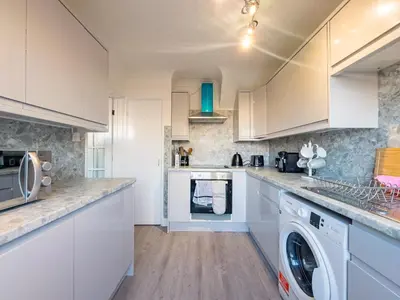 a kitchen with white cabinets and a washer and dryer at House - sleeps 7 private garden & parking in Basildon