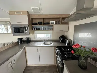 a kitchen with white cabinets and a stove top oven at Your Seaside Escape at St Osyth Modern caravan with decking and wifi and parking Nr to Clacton on Sea in Saint Osyth