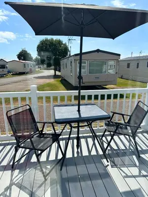a table and two chairs under an umbrella on a deck at Your Seaside Escape at St Osyth Modern caravan with decking and wifi and parking Nr to Clacton on Sea in Saint Osyth