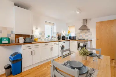 a kitchen with white cabinets and a wooden table with a dining room at Stunning 2 Bedroom Flat with Charming Patio in Cambridge