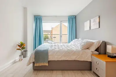 a bedroom with a bed with blue curtains and a window at Stunning 2 Bedroom Flat with Charming Patio in Cambridge