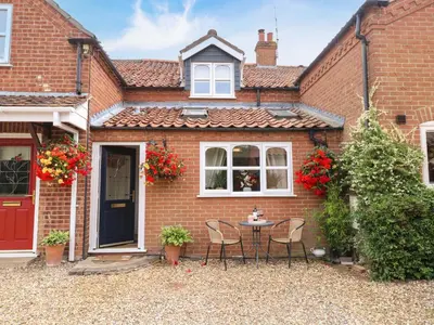 a brick house with a table and chairs in front of it at Honeysuckle Cottage in Swaffham