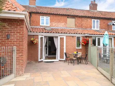 a brick house with a patio with a table and chairs at Honeysuckle Cottage in Swaffham
