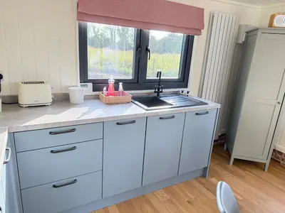 a kitchen with white cabinets and a sink and a window at The Den in Scoulton