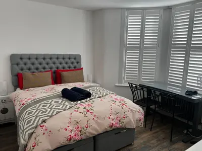 a bedroom with a bed and a desk and windows at Southend Luxe Retreat in Southend-on-Sea