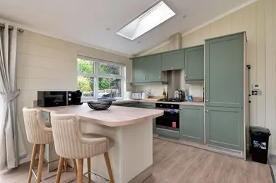 a kitchen with green cabinets and a counter with stools at Finest Retreats - Cambridge Luxury Lodge