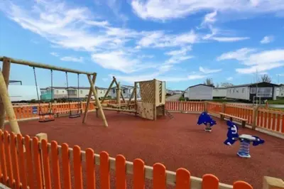an empty playground with an orange fence and swings at Seaside Lodge Haven in St Osyth in Jaywick Sands