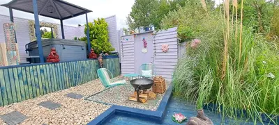 a backyard with a grill and two chairs and a fence at Lily Lake Lodge in Chelmsford