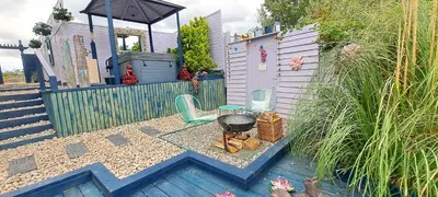 a backyard with a grill and two chairs and a fence at Lily Lake Lodge in Chelmsford