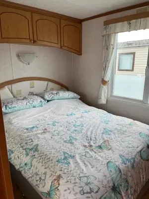 a bedroom with a bed with a comforter and a window at 2 Bedroom Mini Lodge near the beach in Walton-on-the-Naze