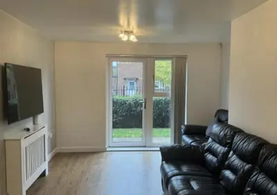 a living room with a black leather couch and a sliding glass door at Hamilton Court in Great Burstead