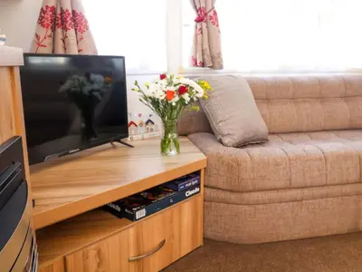 a vase of flowers on a wooden table with a television at 21 Poplar Avenue in Felixstowe