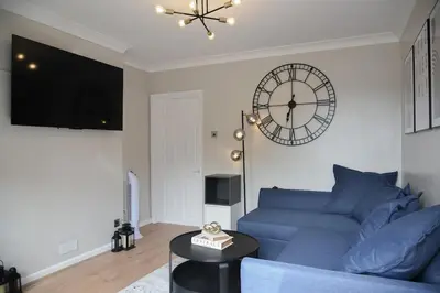 a living room with a blue couch and a clock at Cosy Luxe 3Bed Retreat Hot Tub BBQ Parking Near Town Perfect for Contractors Families Short & Long Stay in Hythe