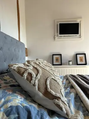 a bed with a pillow and a tv on a wall at Heritage Cottage with a Pool in Diss