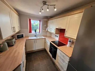 a small kitchen with white cabinets and a window at Seaview house - Three bedroom house with close access to beach by Catchpole Stays in Clacton-on-Sea