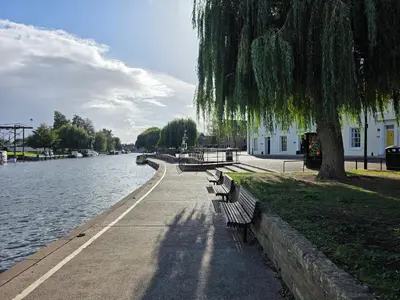 a row of park benches next to a river at Cozy One Bed Flat at Dawe Luxury Suites - An Entire Apartment near Ely Cathedral & Train Station - The Perfect Base to Explore Ely, Cambridge, Norfolk & London - 2 Guests Max & Pet Friendly in Ely