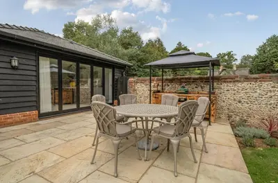 a patio with a table and chairs and an umbrella at Coach House with Hot Tub in Idyllic Bury St Edmunds in Newton