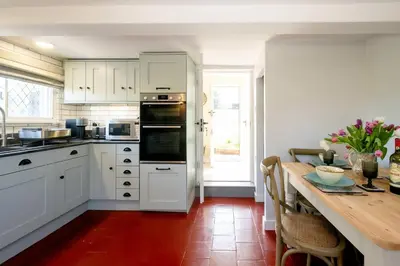 a kitchen with white cabinets and a wooden table at Rose Cottage, Blaxhall - Near Snape Maltings, Orford, Thorpeness & Aldeburgh - Aldeburgh Coastal Cottages in Blaxhall